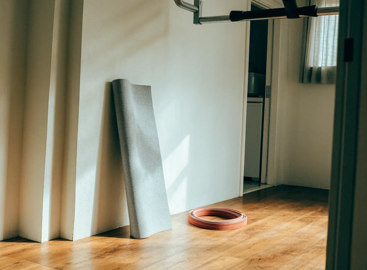A calm home training corner with a folded mat, a coiled resistance band and a doorway pull-up bar